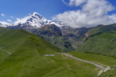 Gürcistan 'da dolambaçlı dağ yolu olan yemyeşil bir vadi üzerindeki Karlı Kazbek Dağı kuleleri..