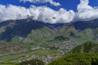Kazbegi kasabası, sarp Kafkas dağlarının ve kalın alçak bulutların altında yeşil bir vadiye yayılır..