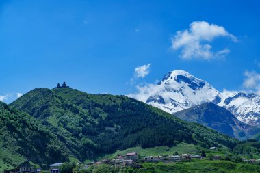 Gergeti Trinity Kilisesi, arkasında karlı Kazbek Dağı 'nın yükseldiği yeşil bir tepeyi taçlandırıyor..