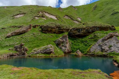 Sakin bir turkuaz havuz, sarp, canlı yeşil bir yamaçtaki engebeli kaya raflarının altında yatar..