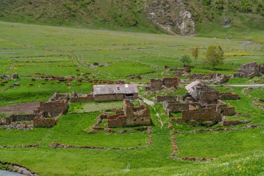 Parçalanmış taş duvarlar, dik yamaçların altındaki yemyeşil bir çayırda eski çiftlikleri izler..