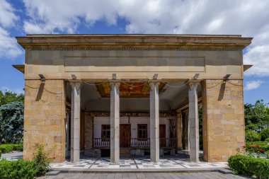 Uzun kolonları olan taş pavyon güneşli müze bahçesinde, Stalin 'in doğduğu ahşap evi koruyor..