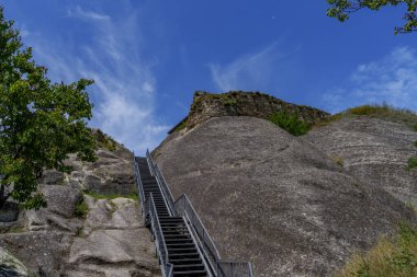 Uzun metal merdivenler dik kayalara tırmanıyor parlak mavi gökyüzünün altında zirveye doğru..