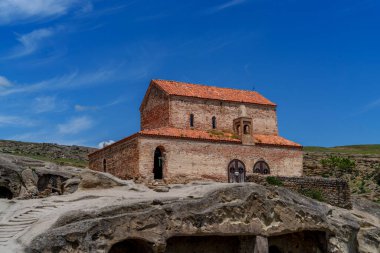 Kırmızı çatılı antik tuğla kilise tarihi Uplistsikhe mağara şehrindeki kaya mağaralarının üzerinde duruyor..