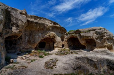 Uplistsikhe mağaralarının antik kumtaşı mağaraları ve odaları incecik bulutların altında güneş ışığında parlıyor..