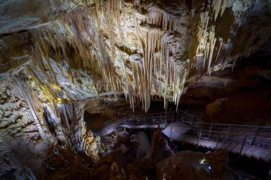 Sarkık sarkıtlarla, dramatik ışıklandırmalarla ve aşağıda küçük bir patikayla dolu büyük bir mağara