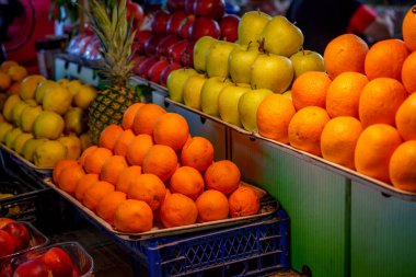 Taze portakallar, elmalar, armutlar ve bir ananas yığını canlı bir meyve standı oluşturur.
