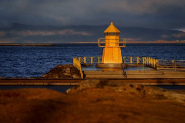 Turuncu deniz feneri, uzak dağlarla gölün üzerindeki kayalık rıhtımda altın saatinde parlıyordu.