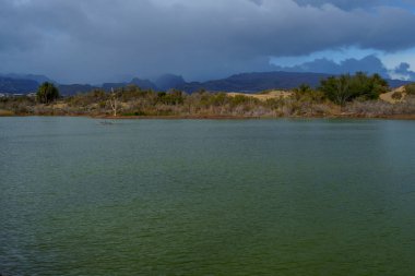Yeşil göl suyu, Büyük Kanarya 'da altın kum tepeleri ve kara bulutlarla buluşur..