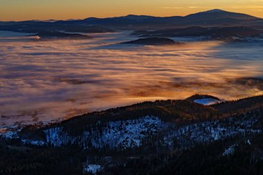 Güneşli sis tersine döner, karlı tepeler ve sıcak bir şafak vakti altında uzak tepelerle dağ vadileri boyunca akar..
