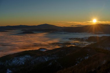 Parlak güneş ışınları ufukta beliriyor, karlı vadilerde ve katmanlı dağlarda sis tersine dönüyor..