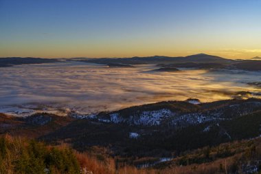 Şafak vakti sisi tersine çevirerek vadileri karlı tepeler ve açık bir gökyüzünün altındaki uzak tepelerle donatır..