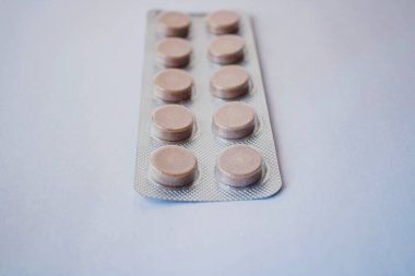 Beyaz arka plandaki paketin içinde yuvarlak bej tıbbi haplar..