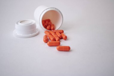 Beyaz arkaplandaki turuncu kapsüller beyaz bir kavanozdan kapakla düştü..