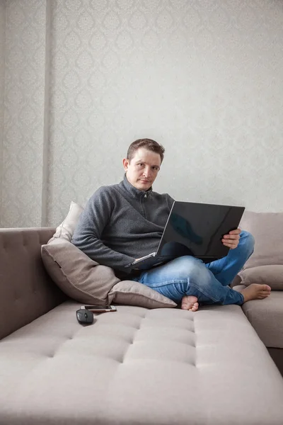 Человек на диване с ноутбуком — стоковое фото