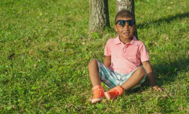 Çimenlerin üzerinde oturan Afro American boy