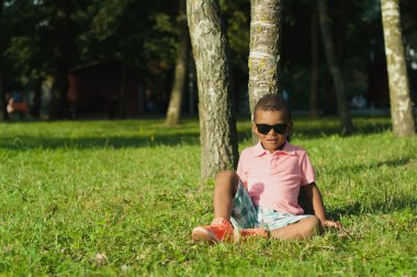 Çimenlerin üzerinde oturan Afro American boy