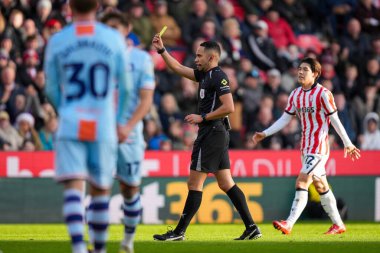 Hakem Ruebyn Ricardo, Stoke City ile Swansea City arasındaki 13 Aralık 2025 'te oynanan Bet365 Stadyumu' nda oynanan Gökyüzü İddia Şampiyonası maçında Swansea City 'den Liam Cullen' a sarı kart gösteriyor.