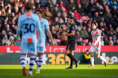 Hakem Ruebyn Ricardo, Stoke City ile Swansea City arasındaki 13 Aralık 2025 'te oynanan Bet365 Stadyumu' nda oynanan Gökyüzü İddia Şampiyonası maçında Swansea City 'den Liam Cullen' a sarı kart gösteriyor.