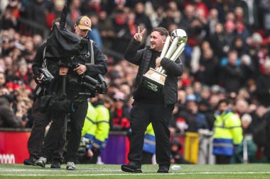 Luke the Nuke Littler, Premier League maçında Manchester United 'a karşı Tottenham Hotspur maçında 7 Şubat 2026 tarihinde Old Trafford, Manchester, İngiltere' de üst üste kazandığı PDC Dünya Şampiyonluğu kupasını gösteriyor.