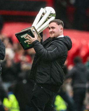 Luke the Nuke Littler, Premier League maçında Manchester United 'a karşı Tottenham Hotspur maçında 7 Şubat 2026 tarihinde Old Trafford, Manchester, İngiltere' de üst üste kazandığı PDC Dünya Şampiyonluğu kupasını gösteriyor.