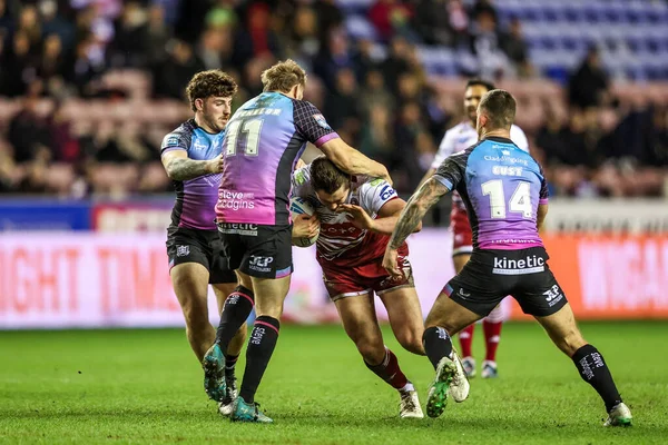 Ethan Havard of Wigan Warriors is tackled by Joe Batchelor of Hull FC and Cade Cust of Hull FC during the Betfred Super League match Wigan Warriors vs Hull FC at The Brick Community Stadium, Wigan, United Kingdom on 21 February 2026