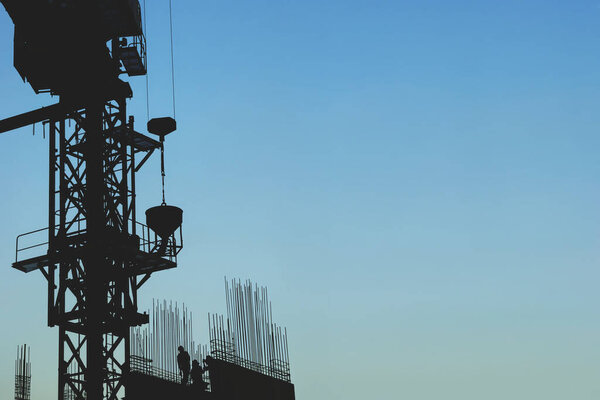 Silhouette of Highrise Crane Lifting Concrete Pourer at a Construction Site