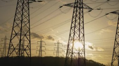 Zaman, günbatımı arka planında pilonlu bir manzara görüntüsü sunar. Yüksek voltajlı elektrik kulesi..