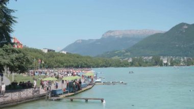 Annecy lac, Annecy, Fransa 'nın panoramik statik görüntüleri. İnsanlar güneşli bir günün tadını çıkarıyor, rıhtımda yürüyor. Arka planda dağ sırtı.