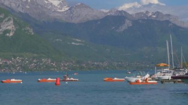 Annecy lac, Annecy, Fransa 'da güneşli bir bahar günü. Suda kayıklar ve pedallar, gölün üstünde yüksek tepeler..