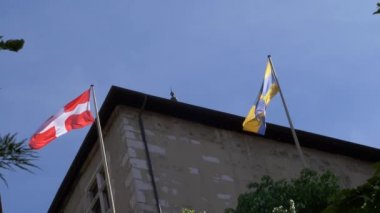 İki bayrak, İsviçre bayrağı, kalenin tepesi ve mavi gökyüzü. Ağır çekimde çekilmiş. Rüzgâr bayrakta.