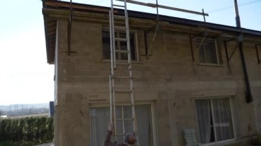 Yavaş çekim gören beyaz erkek işçi, uzun merdivenleri ev yenileme için duvara dayadı. Latin işçiler iş yerindeki merdivenleri dava etti..