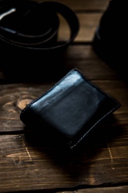 Kahverengi ahşap arka planda siyah deri kemer, cüzdan ve çizmeler kahverengi ahşap arka planda.