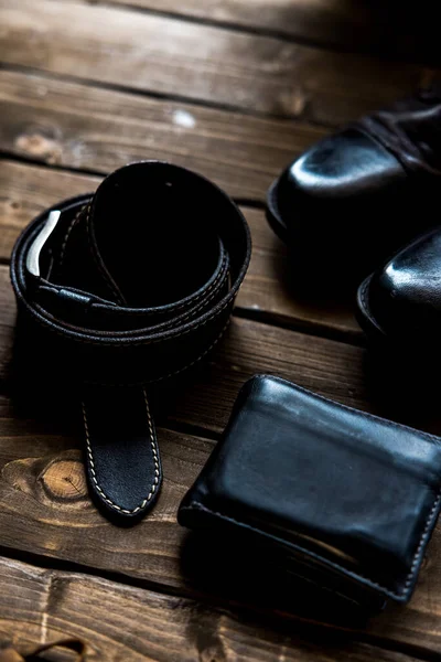 Kahverengi ahşap arka planda siyah deri kemer, cüzdan ve çizmeler kahverengi ahşap arka planda.