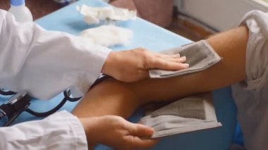 Doktor, eskiden steteskopla yapıldığı gibi tansiyon testi uyguluyor. Erkeklerin kol etrafındaki basınç makinesini büküyor..