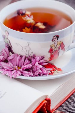 Çiçekli bir kitabın üzerinde duran bitkisel sıcak çay fincanı.
