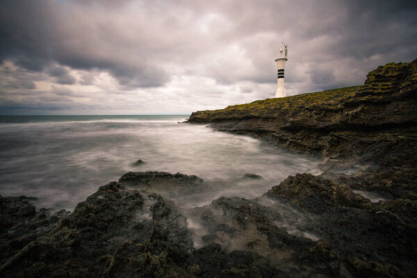 On a day when the waves hit the beach, a wonderful lighthouse looks out over the rocks on a cloudy day.