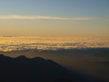 Gün doğumunda bulut denizine karşı dağ siluetleri