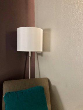 Otel odasının köşesinde sandalye yastığı ve lamba var.