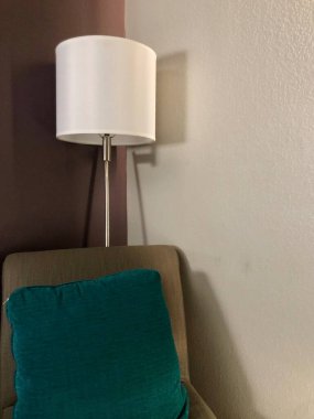 Otel odasının köşesinde sandalye yastığı ve lamba var.