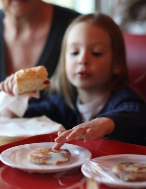 Arka plan bulanık. Küçük kız cheesecake yiyor. Kafe