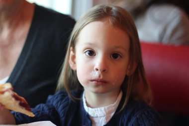 Küçük kız cheesecake yiyor. Yüzü lekelenmiş. Kahvaltını kafede et..