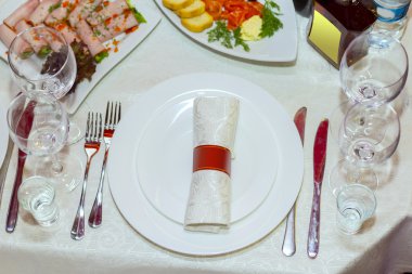 Tablo restoranda, beyaz masa örtüsü ve tabak, çatal ve bıçaklar, gözlük, peçeteler,