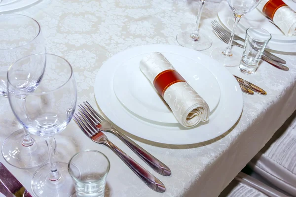 Una mesa en el restaurante, el mantel blanco y platos, tenedores y cuchillos, vasos, servilletas , — Foto de Stock