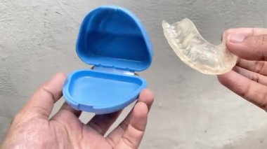 Pürüzsüz ve şeffaf bir TMJ diş bandı dikkatlice mavi bir koruyucu kapta saklanır.