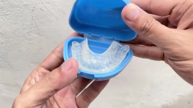 Mavi koruyucu konteynırından açık ve şeffaf bir TMJ diş bandı açılıyor. Bu tıbbi ve diş konsepti çene desteği ve ağız bakımı için kullanılan ortodontik ekipmanları göstermektedir