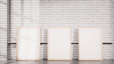 Beyaz tuğla bir duvara karşı yere yerleştirilmiş üç boş çerçeve içeren temiz bir iç modelleme. Marka sunumları, poster koleksiyonları, galeri düzeni, iç tasarım görselleri ve profesyonel pazarlama kullanımı için ideal.