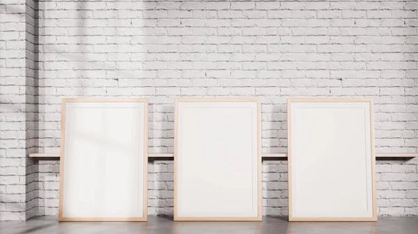 Beyaz tuğla bir duvara karşı yere yerleştirilmiş üç boş çerçeve içeren temiz bir iç modelleme. Marka sunumları, poster koleksiyonları, galeri düzeni, iç tasarım görselleri ve profesyonel pazarlama kullanımı için ideal.