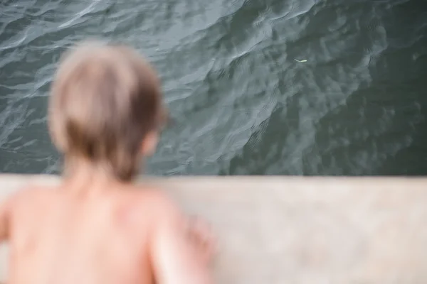 Bambino che abbronza sul ponte di legno al lago nella calda giornata estiva — Foto Stock
