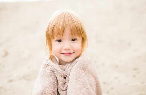 Ragazza bambino con i capelli rossi avvolto in un asciugamano in spiaggia sorridente alla macchina fotografica — Foto Stock